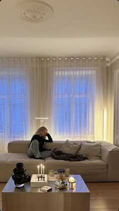 a woman sitting on top of a couch in a living room next to a window