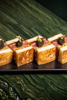 several pieces of food are arranged on a black platter with green marble countertop