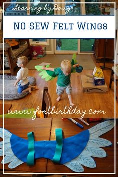 two children play with paper wings on the floor in front of a wooden table and window