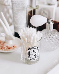 a glass filled with white cotton swabs on top of a counter next to bottles