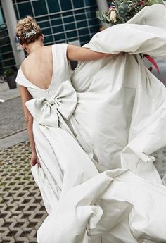 a woman walking down the street in a white dress with a big bow on it's back