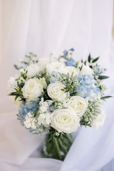 a bouquet of white and blue flowers is sitting on a bed sheet in front of a window