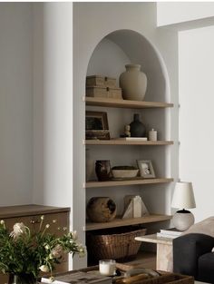 a living room filled with lots of furniture next to a wall mounted book shelf covered in vases and books