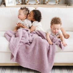 three children laying on a couch with a blanket over them and one is kissing the other