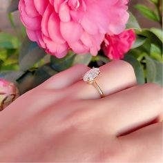 a woman's hand with a ring on it and pink flowers in the background