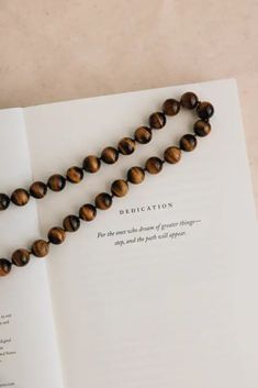 a book with a beaded necklace laying on it's open page and the words dedication written in cursive writing