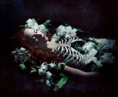 a woman is laying down with flowers in her hair and body, wearing black and white striped dress