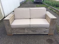 a couch made out of wood sitting on top of a gravel road next to a building