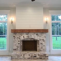 an empty room with a brick fireplace and two windows in the wall, along with a ceiling fan