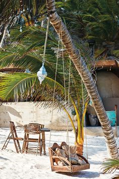 a hammock hanging from a palm tree next to chairs and tables on the beach