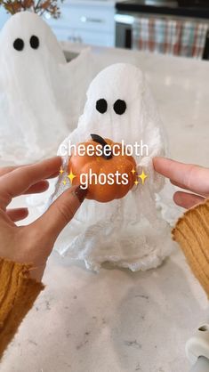 someone is holding a donut in front of two fake ghost heads on a table