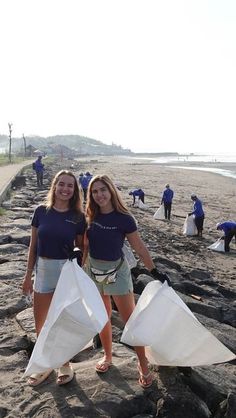 two women standing on the beach holding bags