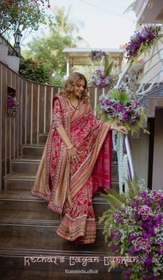 a woman in a red and pink sari is standing on some steps with purple flowers