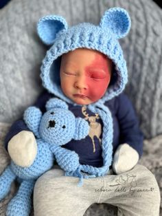 a baby is wearing a blue bear hat and holding a stuffed animal in it's lap