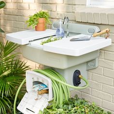 a sink that is sitting in the grass next to a planter and potted plants