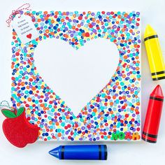 an apple, crayons, and marker are on the table next to a paper heart