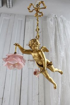 an angel figurine hanging from a chandelier with pink flowers in front of it