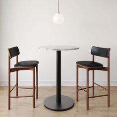 two chairs and a table in a room with wood flooring, one chair has black leather upholstered on the seat