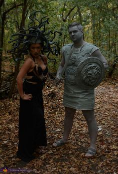 two people standing in the woods with one holding a shield and the other wearing a costume