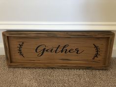 a wooden sign that says gather on the floor next to a carpeted area with white walls