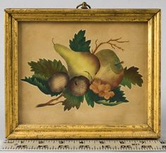 an old painting with fruit and leaves on it in a gold frame next to a ruler