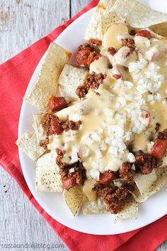 a white plate topped with nachos covered in cheese and chili sauce next to a red napkin