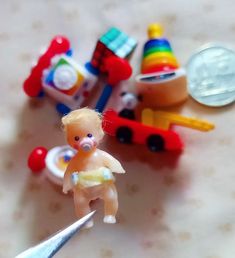 a toy baby doll standing on top of a table next to toys and a pair of scissors