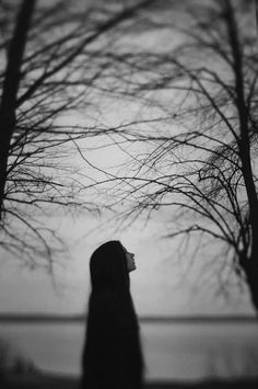 a woman standing in front of some trees with no leaves on it and looking up at the sky