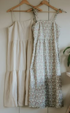 two dresses hanging up against a wall next to a potted plant on a wooden hanger