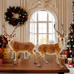 two deer figurines are standing on a table in front of a christmas tree