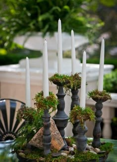 a table with candles, moss and rocks on it in front of an outdoor dining area