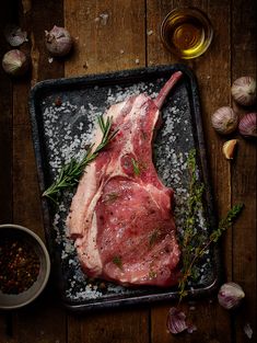 a raw piece of meat sitting on top of a pan next to garlic and seasoning