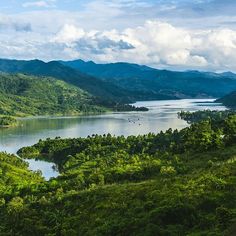 an aerial view of a lake surrounded by lush green trees and mountains in the distance