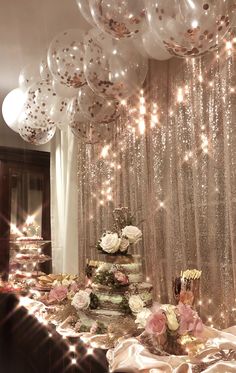 a table topped with lots of white balloons and cake next to a window covered in sequins