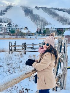 a woman standing on top of a snow covered slope next to a wooden fence with ski slopes in the background