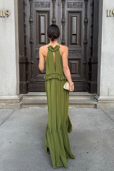 a woman standing in front of a door with her back to the camera, wearing a green dress