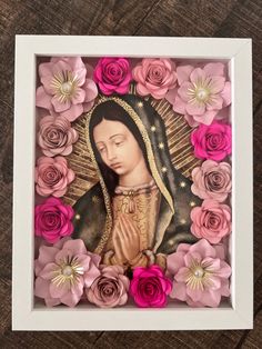 an image of the virgin mary surrounded by pink and purple flowers on a wooden surface