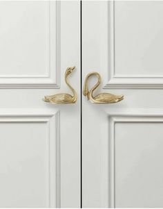 two brass swan hooks on the side of a white door