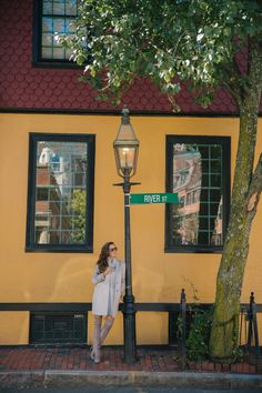 a woman standing next to a lamp post in front of a yellow building with windows