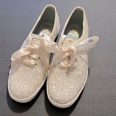 a pair of white tennis shoes with bows on the laces and sequins