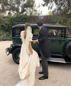 a bride and groom standing in front of an old car