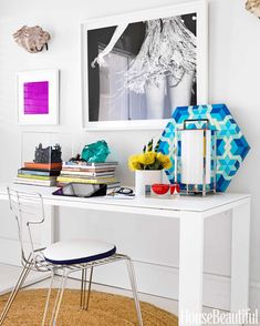 a white desk topped with lots of books next to a chair and pictures on the wall