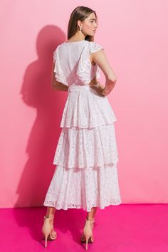 a woman in a white dress is standing against a pink wall with her back to the camera