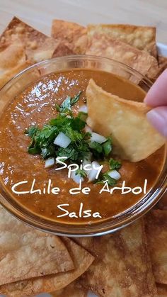 a person dipping tortilla chips into a bowl with salsa in the middle and cilantro on top