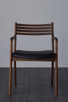 a wooden chair with black leather upholstered seat and back rests on a wood floor