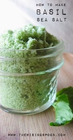 a glass jar filled with green sea salt on top of a wooden table next to leaves