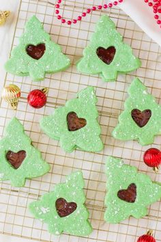 green christmas tree cookies on a cooling rack with ornaments around them and red baubles