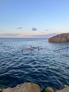 people swimming in the ocean near some rocks