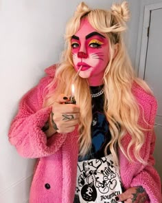 a woman with pink makeup holding a lit candle in her hand while wearing a cat costume