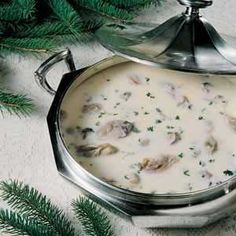 a silver pot filled with soup next to pine branches